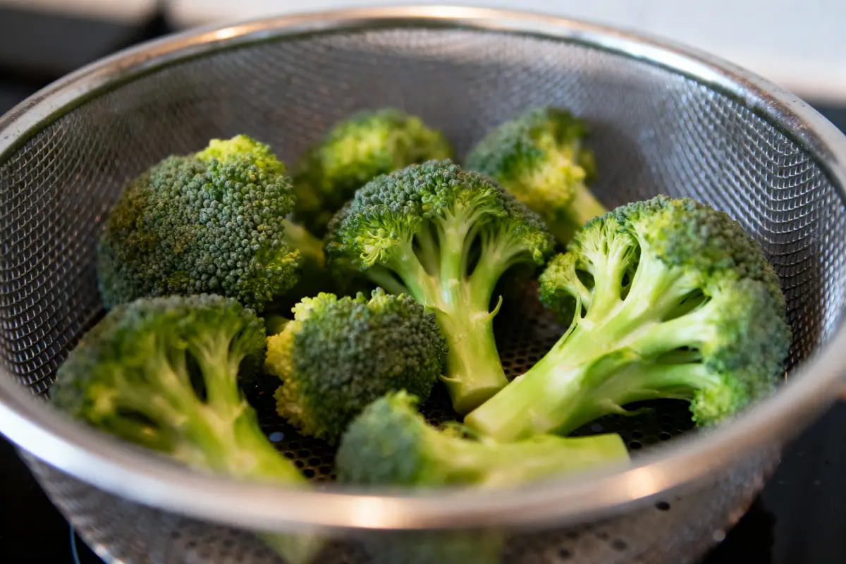 Têtes de brocoli fraîches dans une passoire en acier inoxydable, prêtes pour la cuisson.
